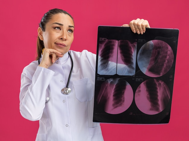困惑して見上げる肺のレントゲン写真を保持している若い女性医師