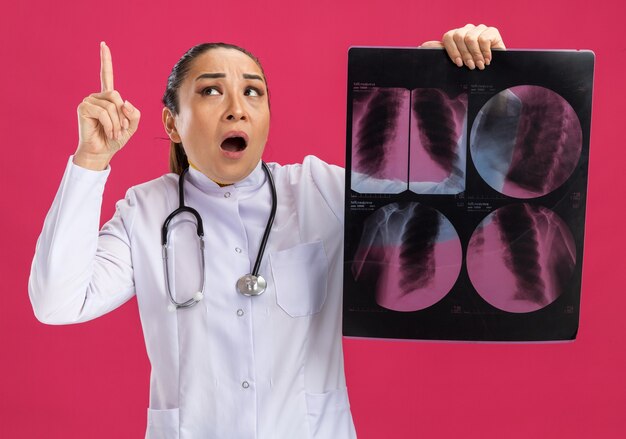 肺のレントゲン写真を持って見上げる若い女性医師は、人差し指が新しいアイデアを持っていることを示して驚いた