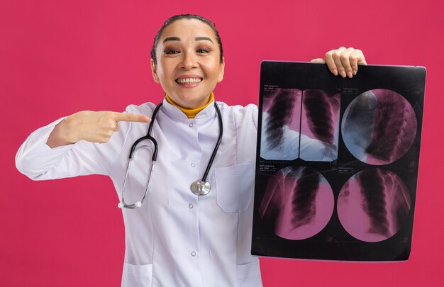 행복하고 긍정적 인 미소에 검지 손가락으로 가리키는 폐의 엑스레이를 들고 젊은 여자 의사