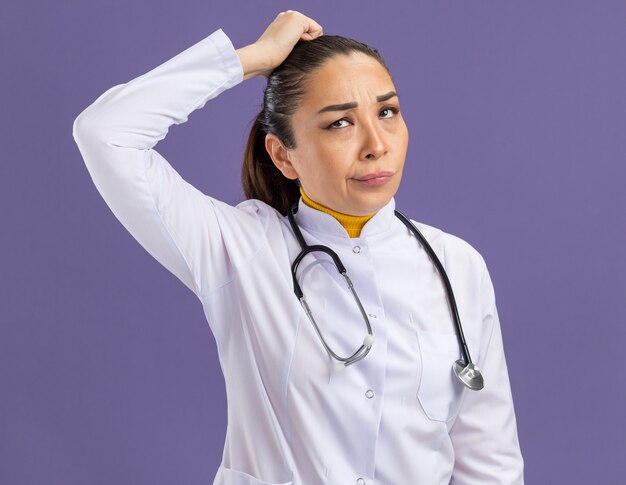 Young woman doctor   looking up puzzled scratching her head