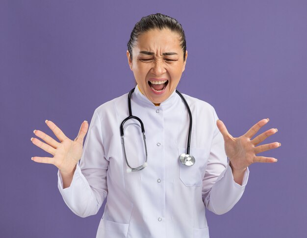 Young woman doctor   shouting with aggressive annoyed expression with arms raised