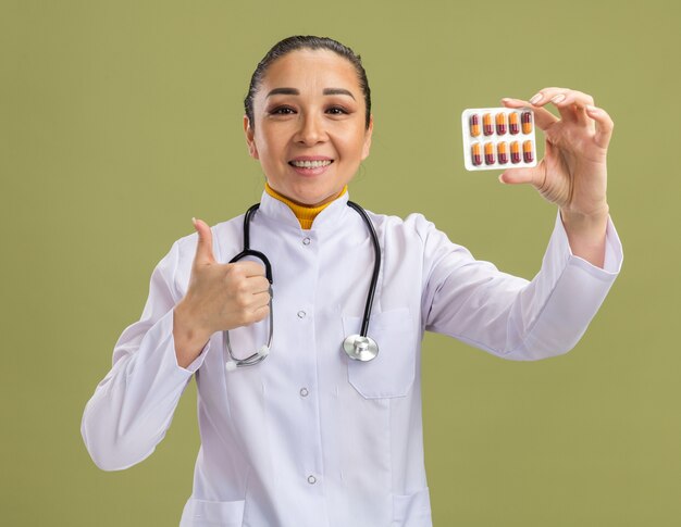 笑顔で親指を示す錠剤と水ぶくれを示す若い女性医師