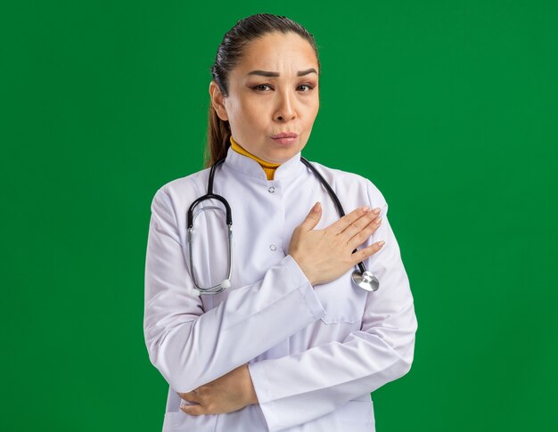 Young woman doctor     with serious face holding hand on chest