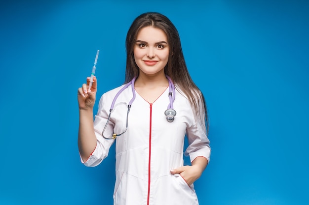 Молодая женщина, врач со шприцем в руке. Портрет среднего плана. Шприц в руке женщины на синем.