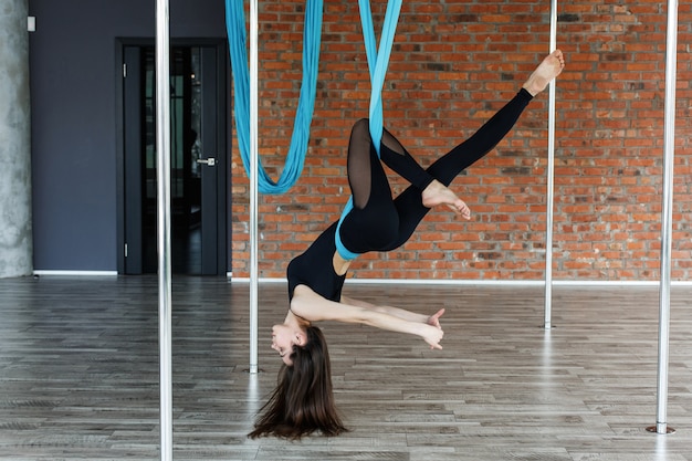 Бесплатное фото Молодая женщина делает воздушную йогу на голубой висит гамак в тренажерном зале