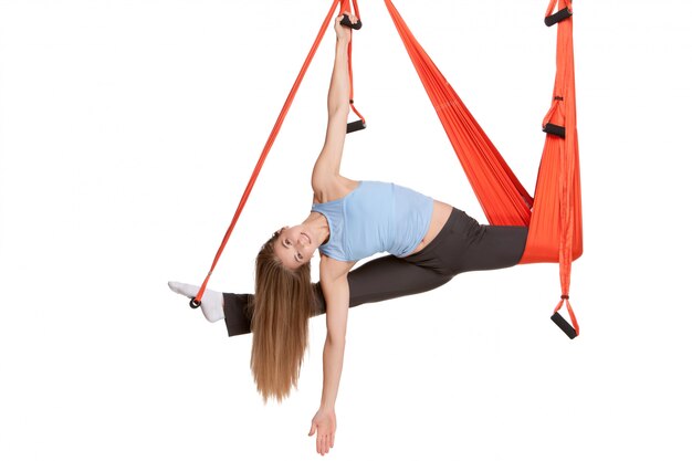 Young woman doing anti-gravity aerial yoga in hammock on a seamless white wall