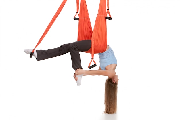 Young woman doing anti-gravity aerial yoga in hammock on white wall