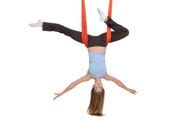 Young woman doing anti-gravity aerial yoga in hammock on white wall