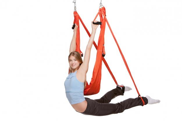 Young woman doing anti-gravity aerial yoga in  red hammock on a seamless white wall