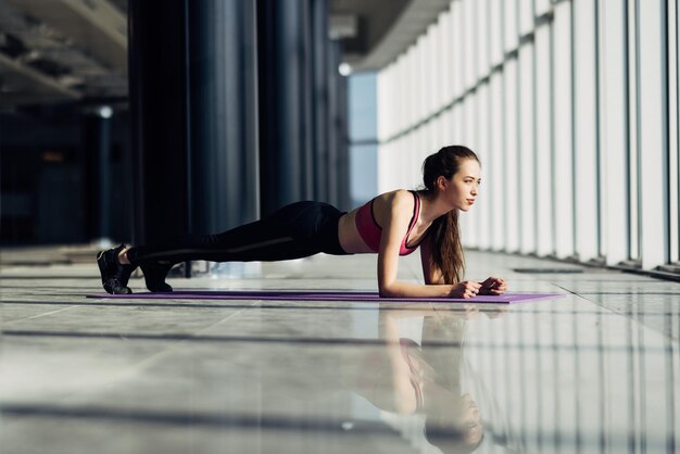 Молодая женщина делает упражнения на фитнес-коврик в тренажерном зале. Подходящая женщина делает отжимания во время тренировки в оздоровительном клубе.