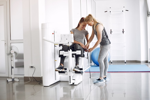 Free photo young woman doing exercises on simulator with therapist in gym