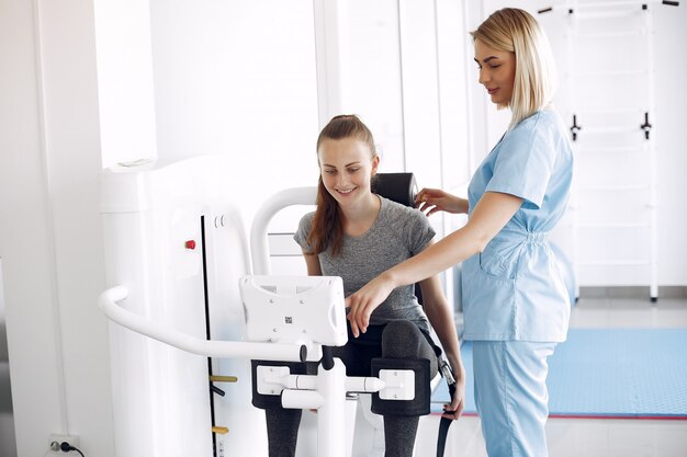 Young woman doing exercises on simulator with therapist in gym