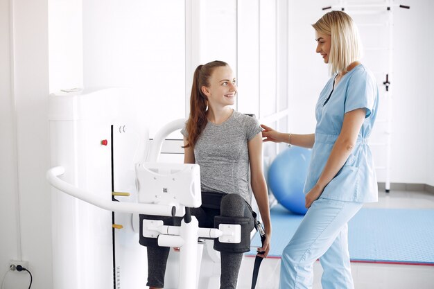 Young woman doing exercises on simulator with therapist in gym