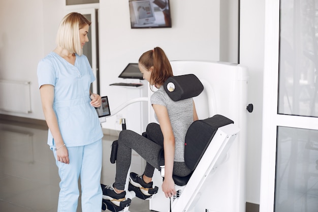 Young woman doing exercises on simulator with therapist in gym