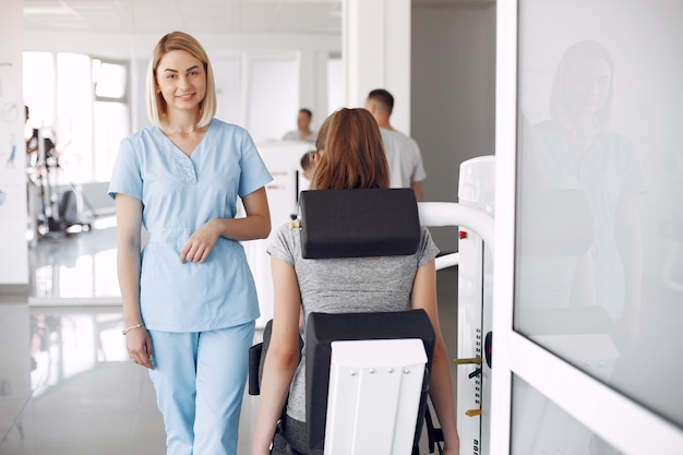 Young woman doing exercises on simulator with therapist in gym