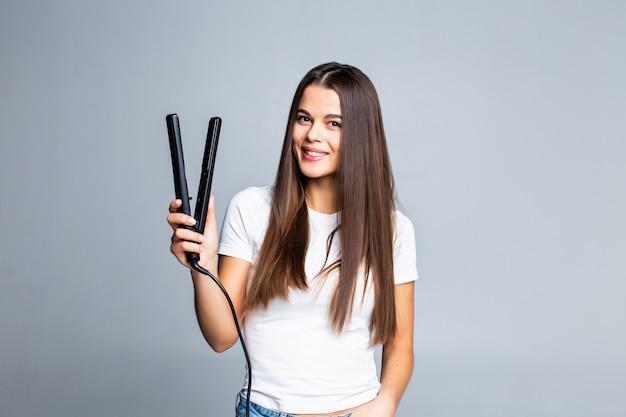 Young woman doing hairstyle with hair straightener isolated on gray