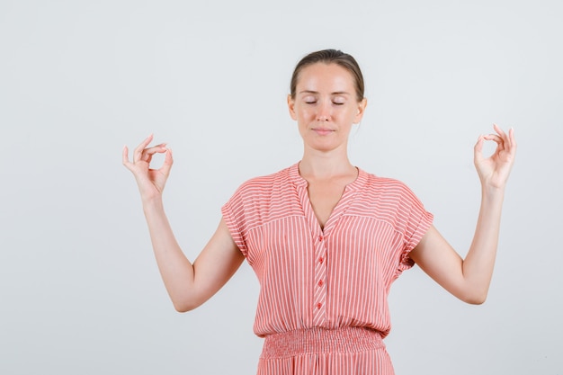 Young woman doing meditation with closed eyes in striped dress and looking relaxed. front view.