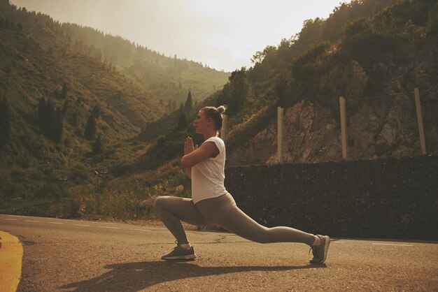Молодая женщина делает упражнения на растяжку на природе в горах. спортивная девушка, практикующая йогу, позирует в леггинсах и кроссовках, красивый лесной пейзаж