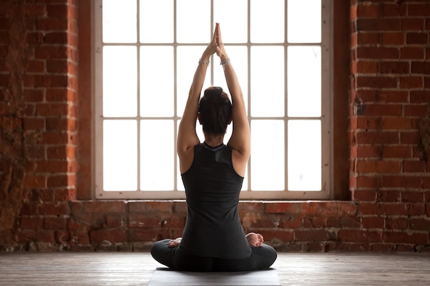 Young woman doing Sukhasana exercise, rear view