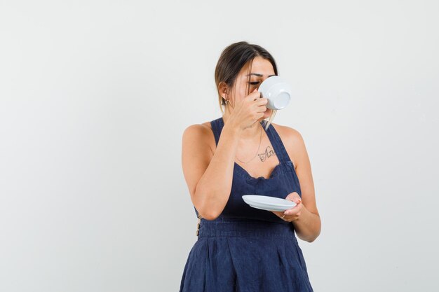 Young woman in dress drinking aromatic tea and looking delighted