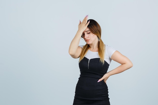 Young woman in dress holding hand on forehead and looking exhausted