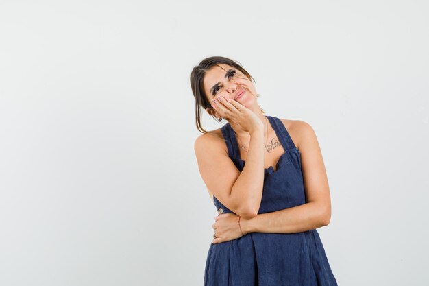 Young woman in dress leaning cheek on palm and looking pensive