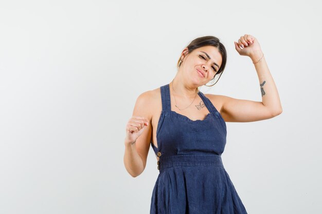 Young woman in dress showing success gesture and looking blissful