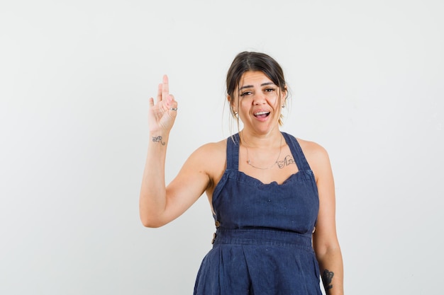 Young woman in dress showing three fingers of hand and looking amazed