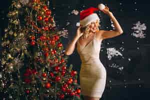 Free photo young woman in dress with christmas presents by christmas tree
