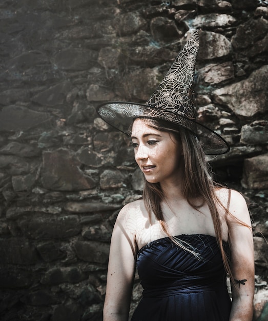 Free photo young woman in dress and wizard hat looking aside