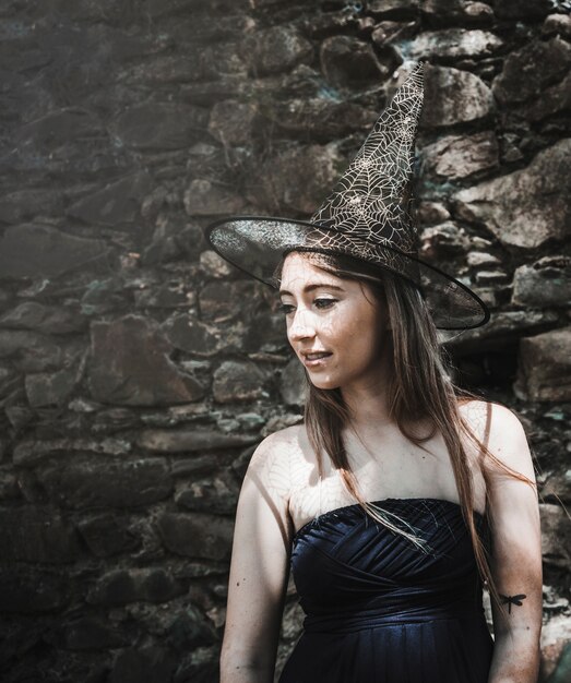 Young woman in dress and wizard hat looking aside