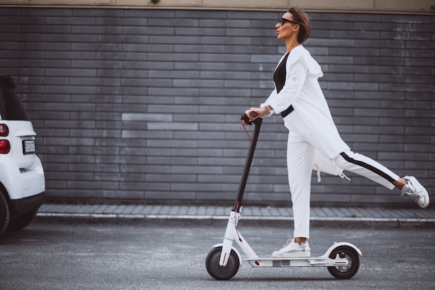 Young woman dressed in white riding scooter