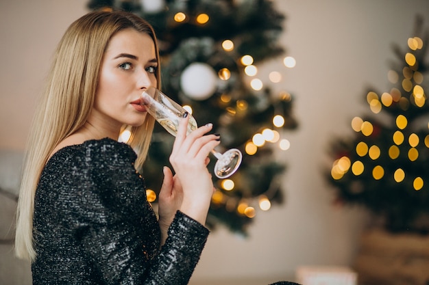 Молодая женщина пьет шампанское у елки