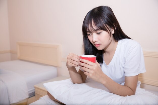 젊은 여자가 그녀의 침대에서 집에서 커피를 마시고 그녀의 노트북을 확인