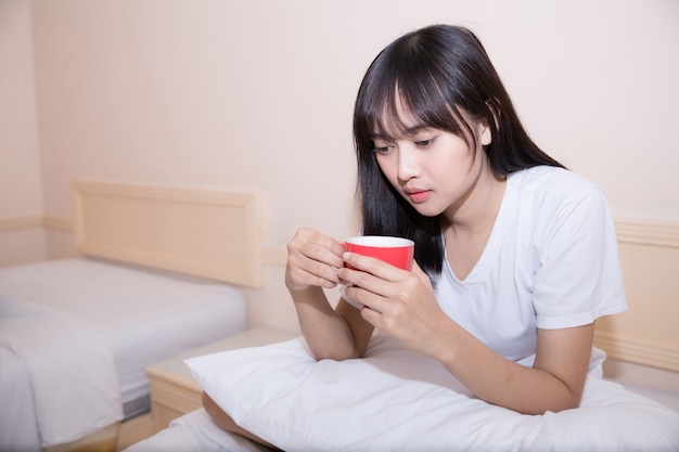 Young woman drinking coffee at home in her bed and checking her laptop