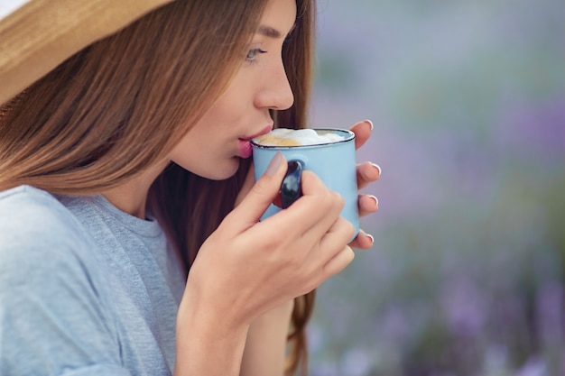 Молодая женщина пьет кофе в поле лаванды