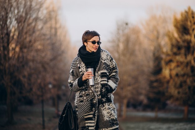 Молодая женщина пьет кофе утром и гуляет в парке