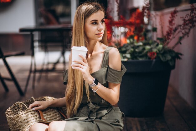 カフェの外でコーヒーを飲む若い女性
