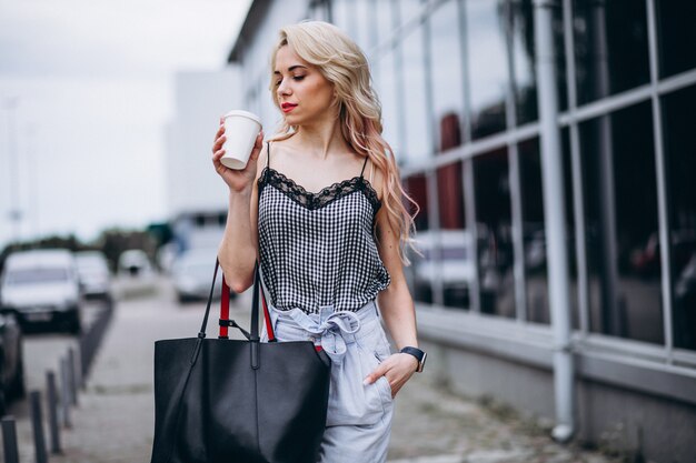 若い女性が通りの外のコーヒーを飲む