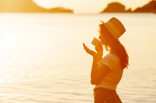 Caffè bevente della giovane donna sul tramonto