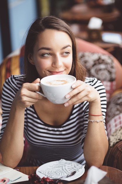 Free photo young woman drinking coffee in urban cafe