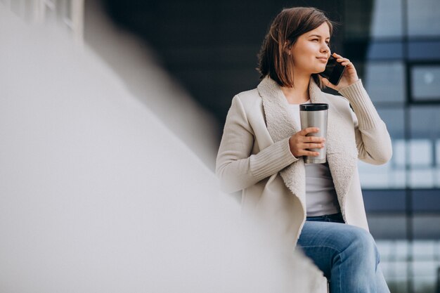 コーヒーを飲みながら通りの外で電話を使用して若い女性