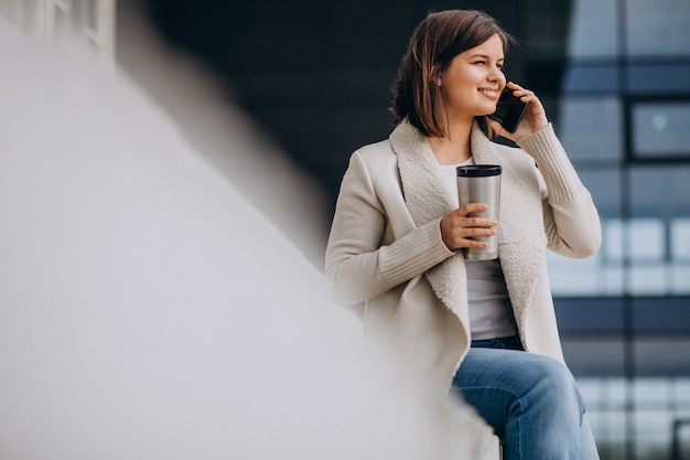Молодая женщина, пить кофе и с помощью телефона за пределами улицы