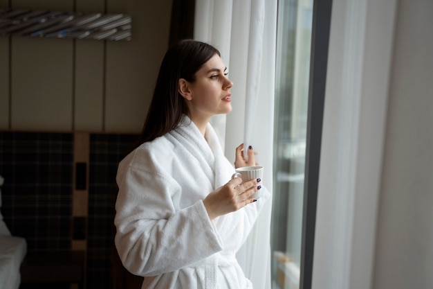 ホテルの部屋のベッドに座ってコーヒーを飲む若い女性