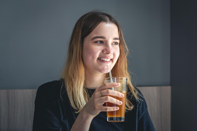 A young woman drinking cold summer coffee drink with ice and orange juice