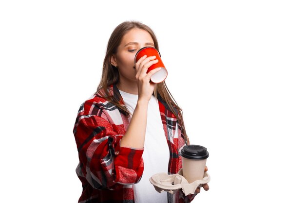 Молодая женщина пьет чашку кофе, держа на вынос держатель с чашкой, белый фон