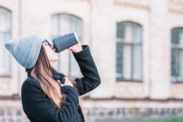 Young woman drinking from cup on street 