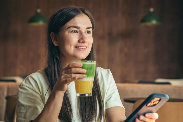 A young woman drinking lemonade and using a smartphone in a cafe