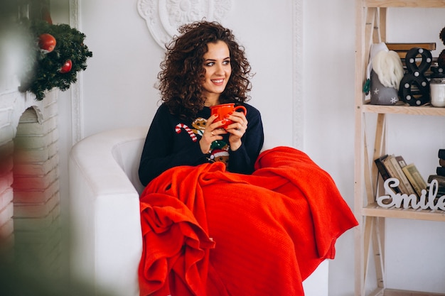 Giovane donna che beve il tè dall'albero di natale