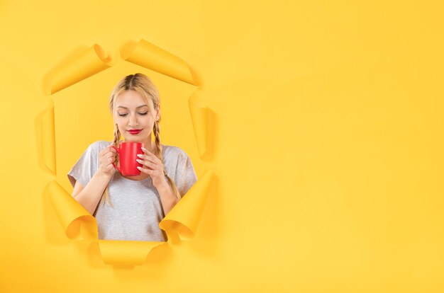 Young woman drinking tea on torn yellow paper background facial advertising shopping